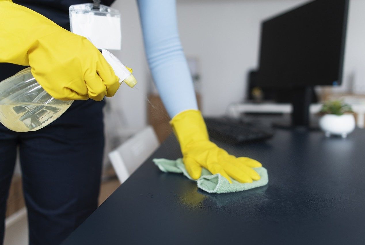Nettoyage des surfaces Main dans un gant bleu nettoyant une surface avec un chiffon gris, éponge jaune en arrière-plan.